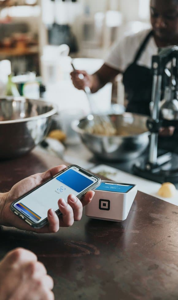 A hand tapping a phone to pay on a POS card reader